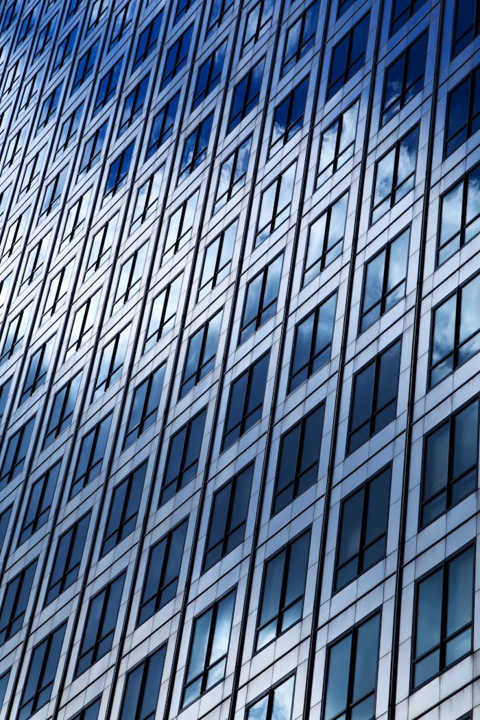 Close-up of a modern glass skyscraper reflecting clouds on a clear day.