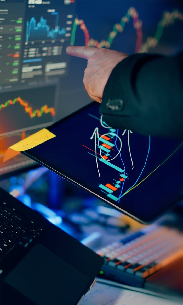 about-02 A business professional examines financial charts on a tablet and monitor for investment strategy.